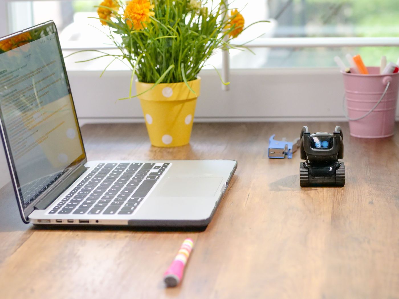 A laptop on a desk beside flowers and a small friendly robot, standing in for the AI tools customers now ask for recommendations.